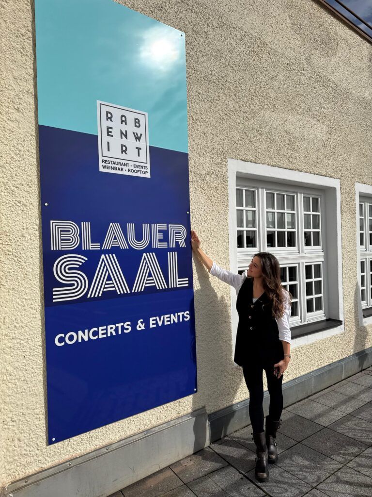Chiara Abenteuer steht vor einem Plakat des Blauen Saals