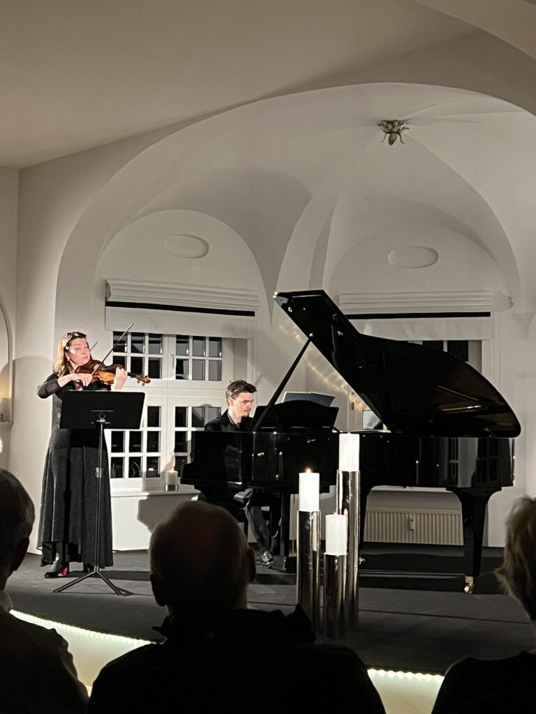 Ein Pianist spielt am Flügel, eine geigerein steht daneben und spielt ebenfalls
