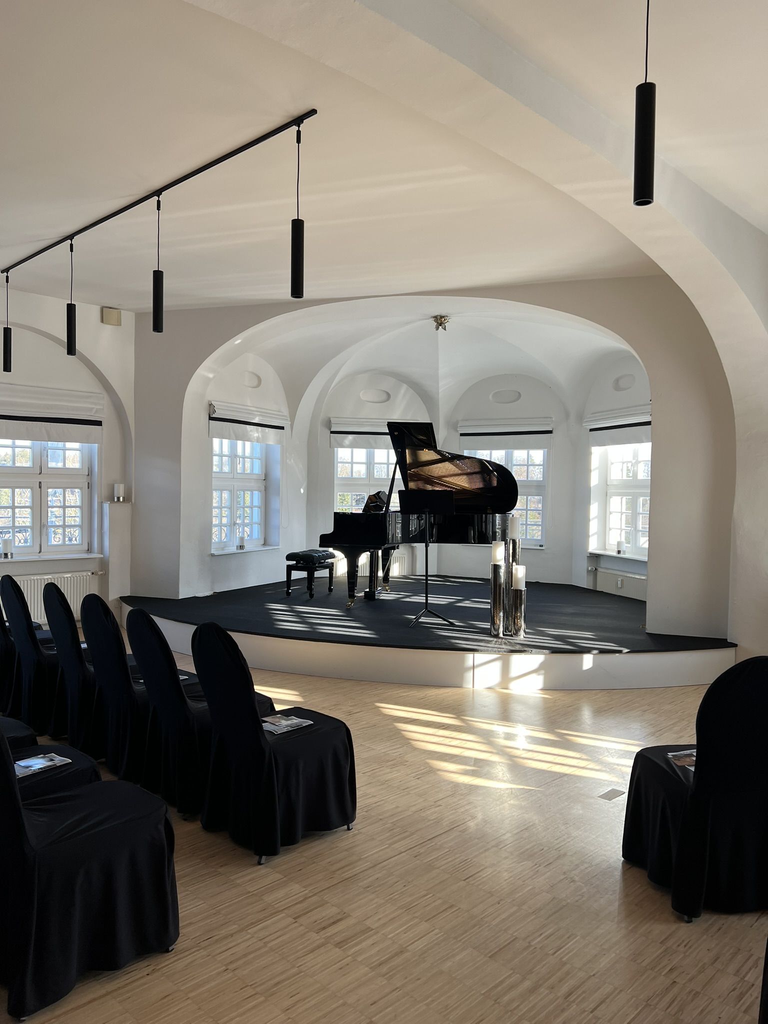 Blick vom Zuschauerraum eines sonnendurchfluteten kleinen Konzertsaals auf eine kleine Bühne mit Flügel