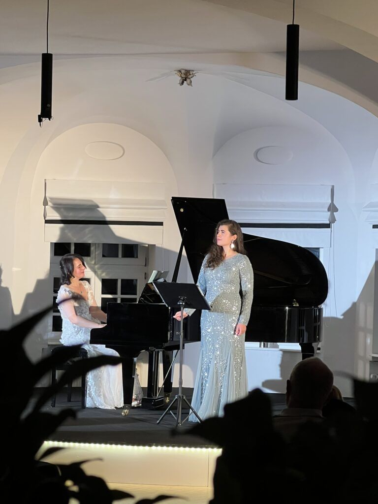 Eine Pianistin spielt auf einem Flügel, eine andere steht singend daneben